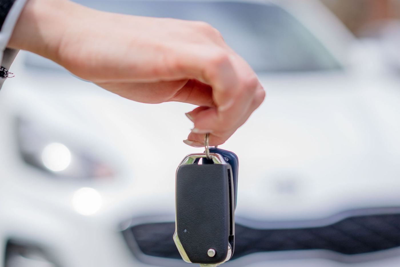 Mão segurando a chave de um carro branco